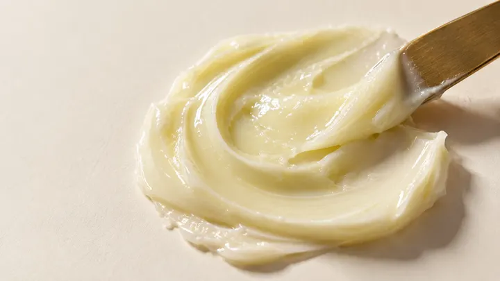 Textura de una crema clara extendida con una espátula dorada